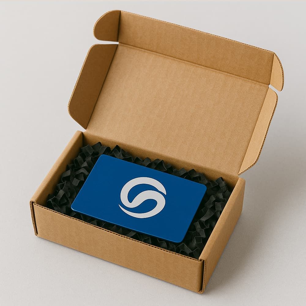 Otwarty kartonik wypełniony czarną przekładką, w środku tabliczka grawerowana w kolorze niebieskim z białym sygnetem — gotowa do bezpiecznej wysyłki.